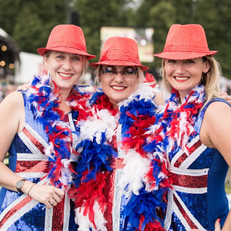 Three women in patriotic costumes with red hats and feather boas at Pennywood Tours event.