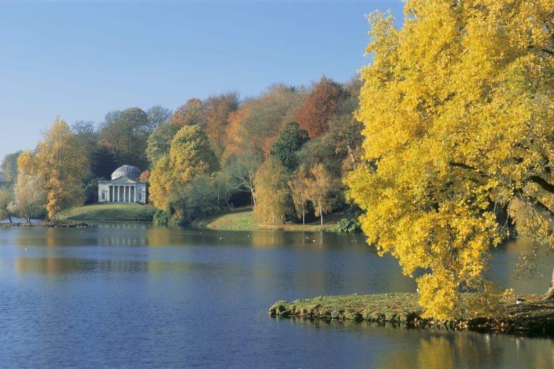 Beautiful autumn landscape with lake, trees, and a white pavilion in the distance.