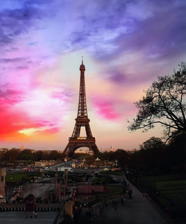 Eiffel Tower during sunset with colorful sky and surrounding park.