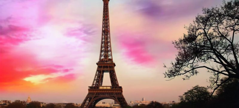 Eiffel Tower during sunset with colorful sky and surrounding park.