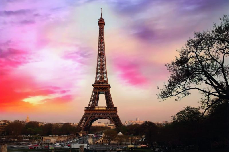 Eiffel Tower during sunset with colorful sky and surrounding park.