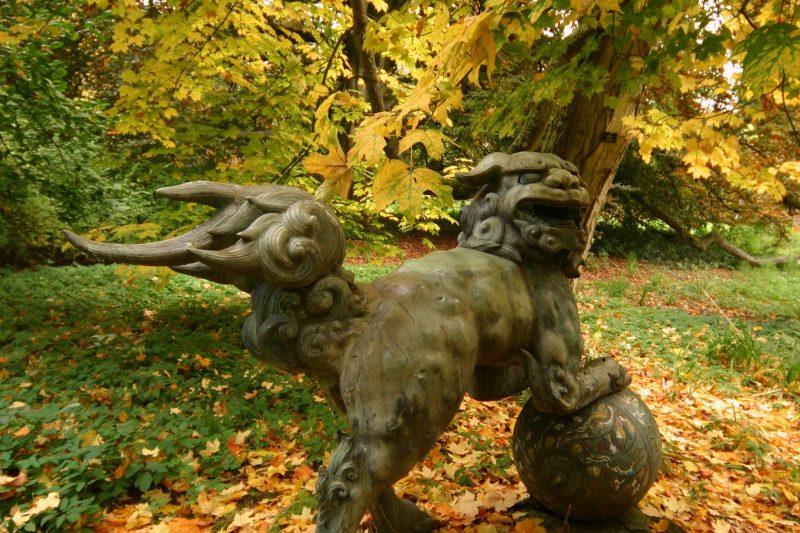 Bronze dragon sculpture in autumn park with colourful leaves and trees.