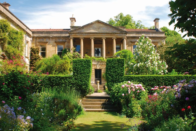 Beautiful historic mansion surrounded by lush garden and vibrant flowers.