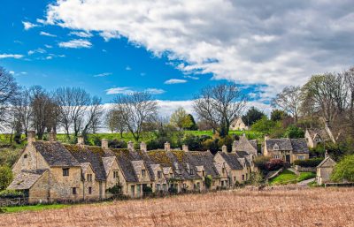 Picturesque village with stone cottages and lush trees under a blue sky.
