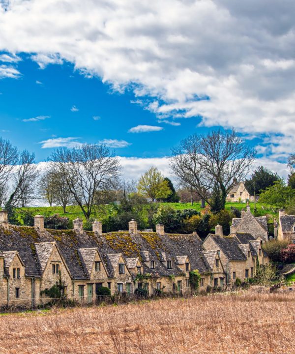 Picturesque village with stone cottages and lush trees under a blue sky.