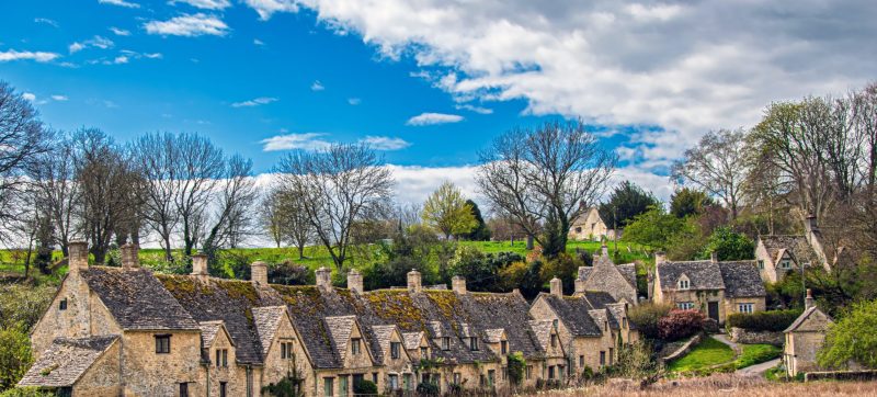 Picturesque village with stone cottages and lush trees under a blue sky.