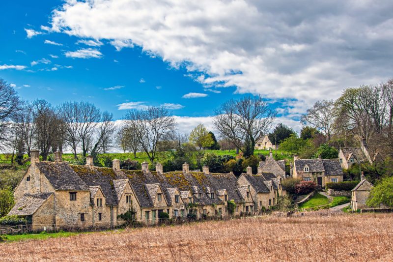 Picturesque village with stone cottages and lush trees under a blue sky.