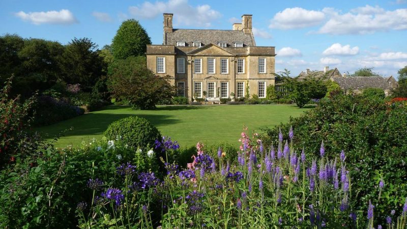 Elegant historic mansion surrounded by lush gardens and vibrant flowers.